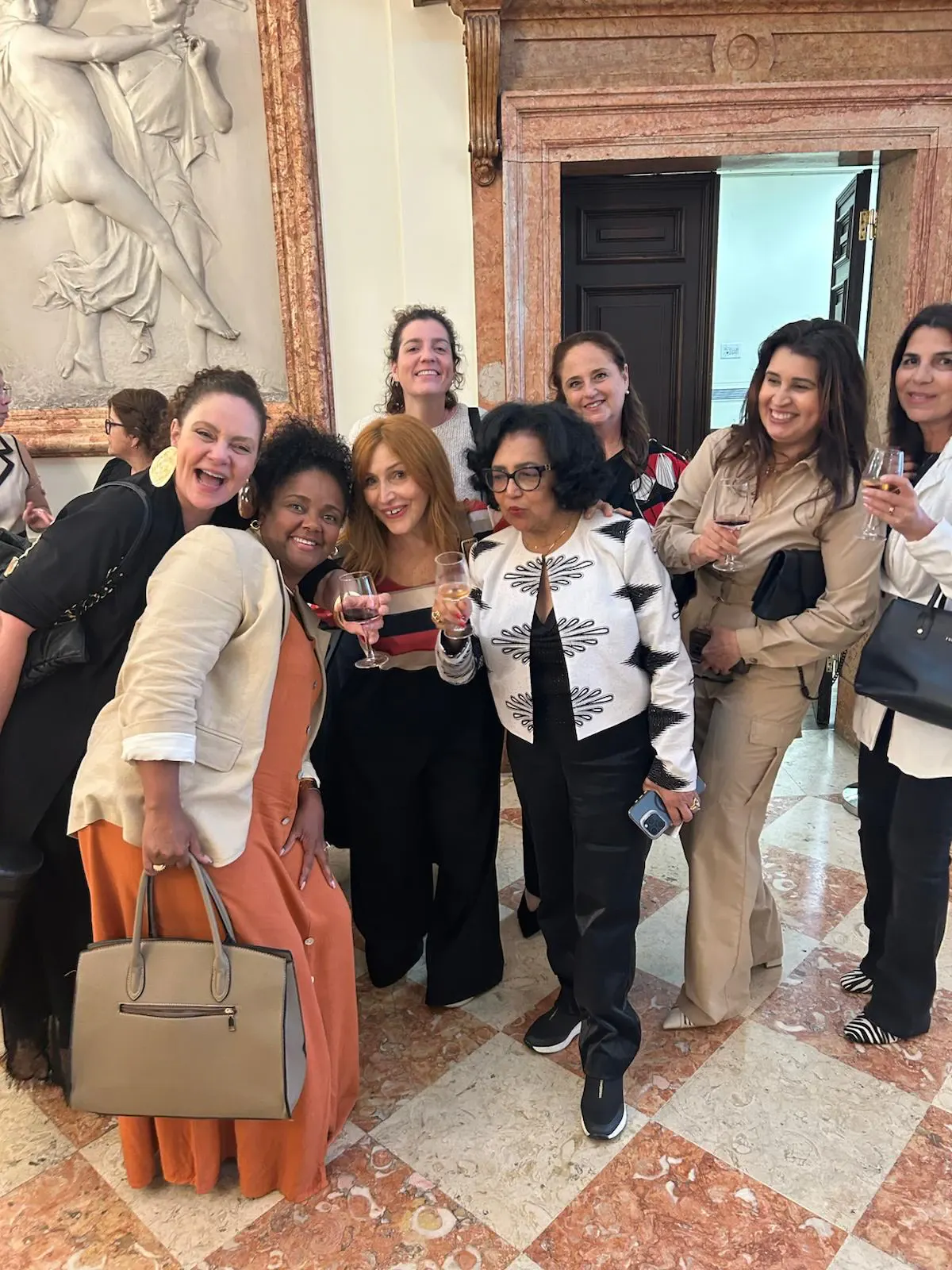 Aline Souza com um grupo de convidadas num salão com piso de mármore.