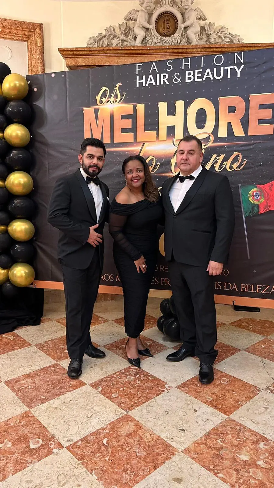 Aline Souza com dois convidados diante do painel “Os Melhores do Ano”, da Fashion Hair & Beauty.