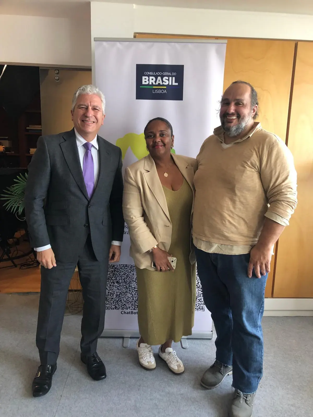 Aline Souza com dois convidados junto ao painel do Consulado-Geral do Brasil em Lisboa.