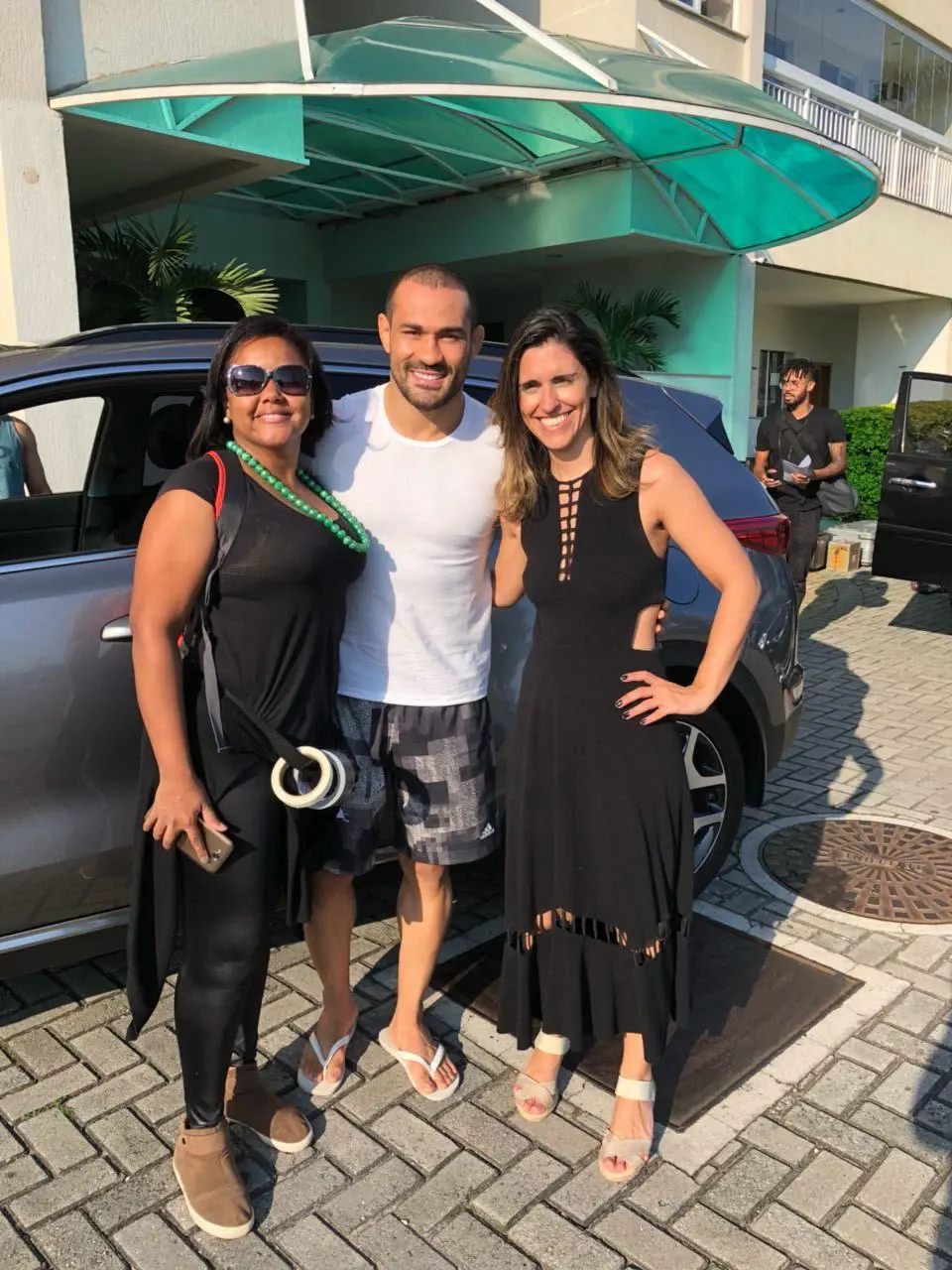 Aline Souza com dois convidados à porta de um edifício.