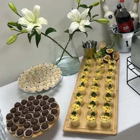 Mesa de doces com brigadeiros e copinhos de mousse, decorada com lírios brancos.