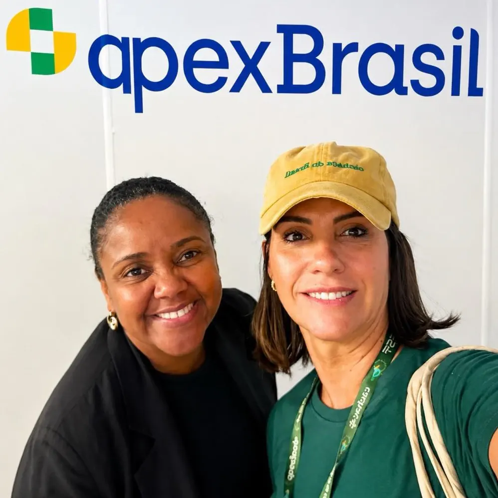 Aline Souza com uma convidada junto ao logótipo da ApexBrasil, em Lisboa.